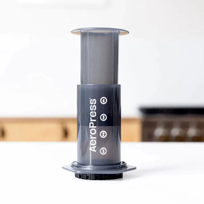AeroPress vertical con cámara transparente y base negra con indicadores para preparar café