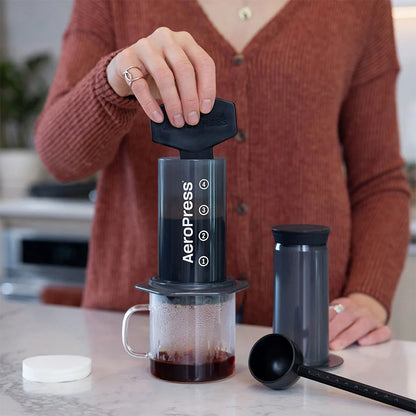 AeroPress en mesa con cafetera y filtro negro, cámara transparente con café