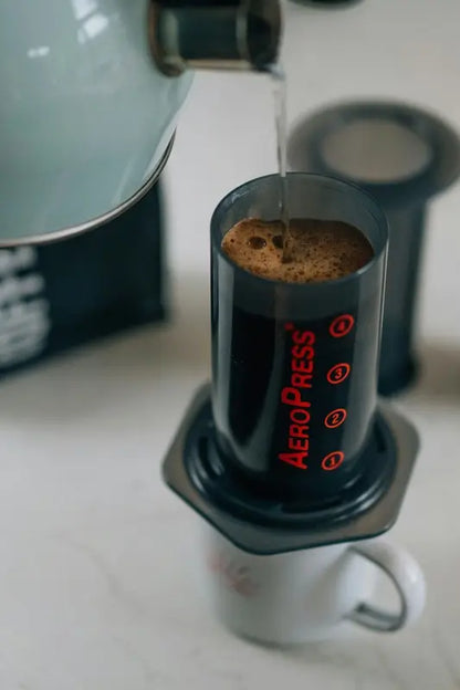 AeroPress con café colado en la taza, filtro negro y cámara transparente