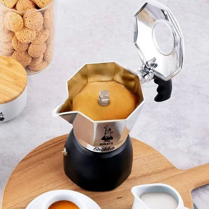 Cafetera italiana Moka con base negra y depósito de acero octagonal, vertiendo café.