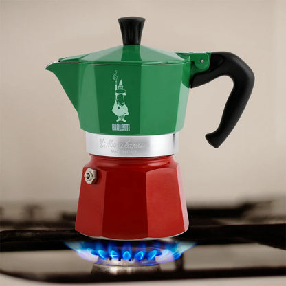 Cafetera moka tricolor roja y verde con asa negra, preparada sobre placa