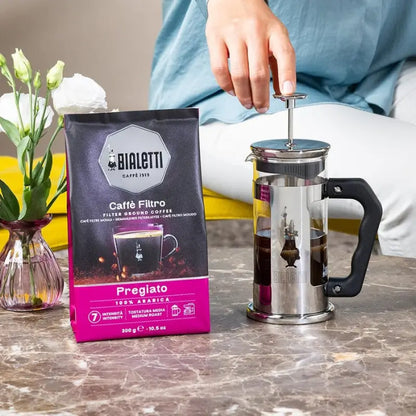Bolsa de café molido Bialetti Pregiato y cafetera de acero con mano sobre el émbolo