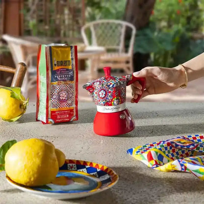 Cafetera moka roja de inducción con tapa roja y diseño multicolor sobre encimera exterior