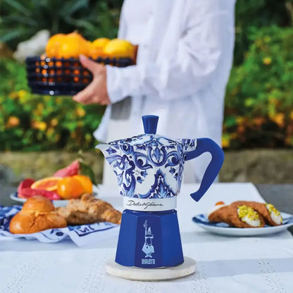 Cafetera moka Bialetti Dolce&Gabbana azul en mesa con tazas y vasos decorados