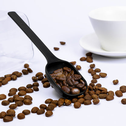 Cuchara de café negra con granos de café en la pala y mango largo