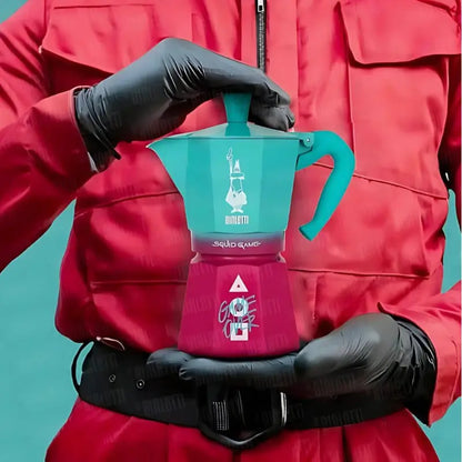 Cafetera moka turquesa y magenta con asa lateral y tapa superior, vista frontal