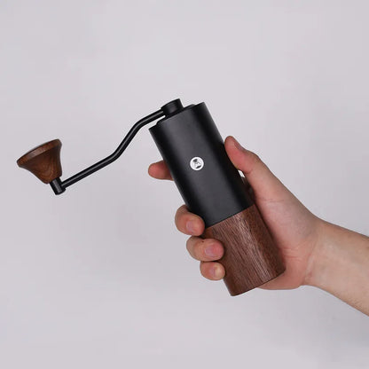 Molino de café negro con base de madera y manivela, sujeto con la mano