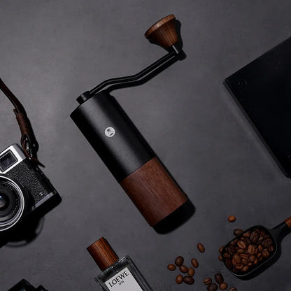Molino de café negro con base de madera y manivela, con granos de café alrededor