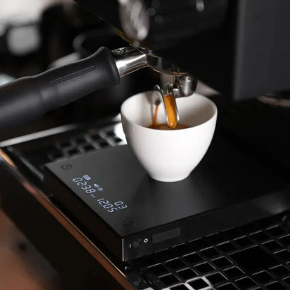 Balanza electrónica negra en uso, con taza blanca bajo el dispensador