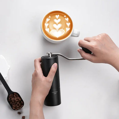 Molino de café negro vertiendo sobre taza, con mano sujetando el cuerpo del molinillo