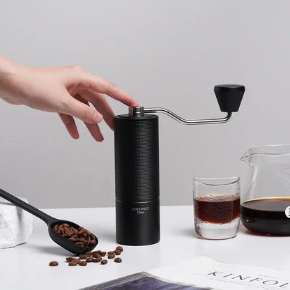 Molino de café negro con manivela y tapa superior, con granos alrededor