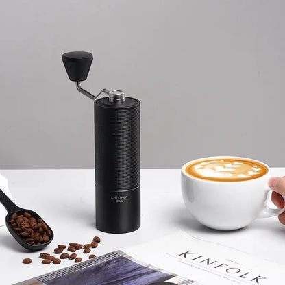 Molino de café negro alto con manivela; junto a granos y taza de café