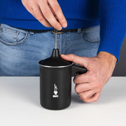 Espumador de leche negro Bialetti en uso, con tapa y asa sujetadas por manos