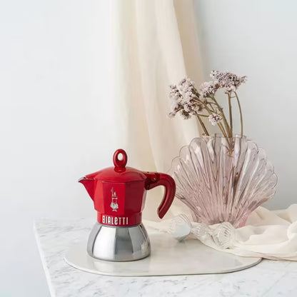 Cafetera moka de inducción roja Bialetti sobre bandeja blanca, con base metálica.