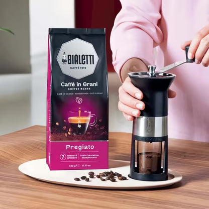 Bolsa de café en grano Bialetti junto a un molino manual