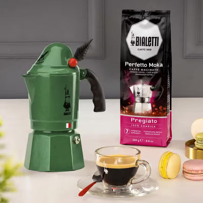Cafetera moka Bialetti Alpina verde de 3 tazas con asa negra, con taza de café.