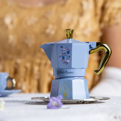 Cafetera moka azul celeste con asa dorada y dibujo floral, vista frontal