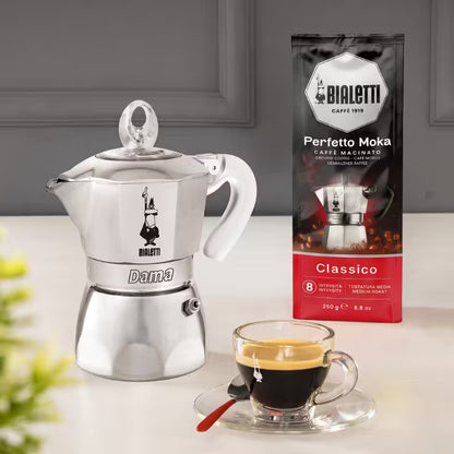 Cafetera Bialetti Dama de acero con taza de café al frente y paquete