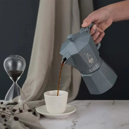 Cafetera moka octogonal azul vertiendo café en una taza blanca