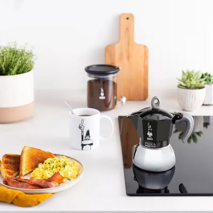 Cafetera italiana moka Bialetti negra con taza de café servida
