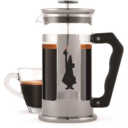 Prensa francesa Bialetti de acero inoxidable con asa negra y jarra de vidrio con café al fondo