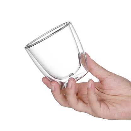 Vaso de vidrio de doble pared transparente sostenido por una mano, vista inclinada