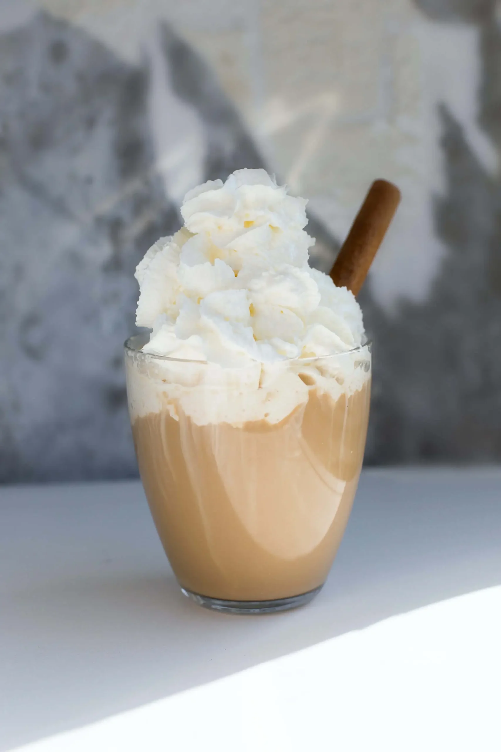Un vaso de café helado con crema y un palo de canela, ideal para disfrutar en un día caluroso.