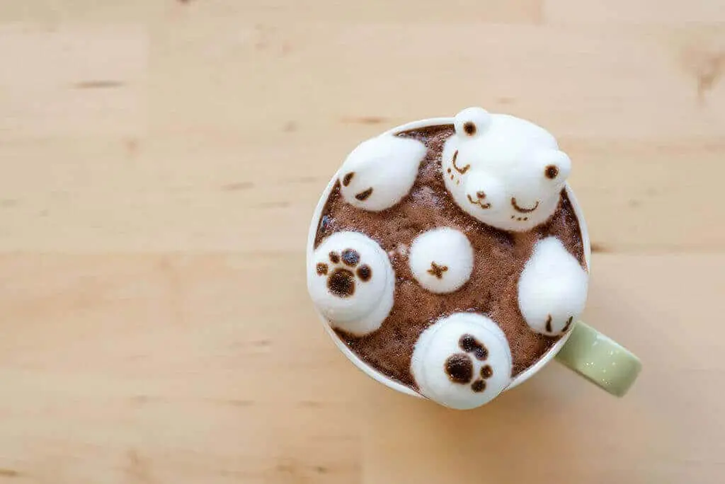 Taza de chocolate caliente con marshmallows y un dibujo de un oso en la superficie, decorada con arte latte.