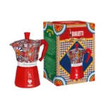 Cafetera italiana roja Bialetti con diseño de carretos sicilianos, acompañada de su caja de empaque decorada.