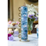 Elegante juego de té azul y blanco en una mesa, con tazas de porcelana y un soporte dorado que evoca el estilo Bridgerton.