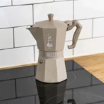Cafetera Italiana Moka Octagonal sobre una cocina de inducción, con un elegante fondo de azulejos en blanco.